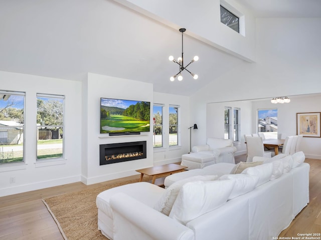 living area featuring beamed ceiling, a warm lit fireplace, light wood-style floors, a notable chandelier, and high vaulted ceiling