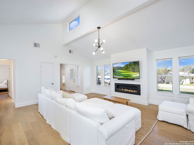 living area with visible vents, baseboards, a glass covered fireplace, and light wood-style flooring