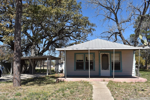 bungalow-style home featuring a porch, a carport, a front yard, and metal roof