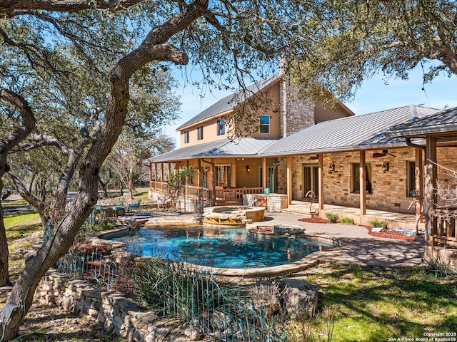 back of house with metal roof, a chimney, a patio area, an in ground hot tub, and a standing seam roof