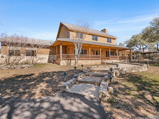 view of front of house featuring covered porch, a chimney, and metal roof