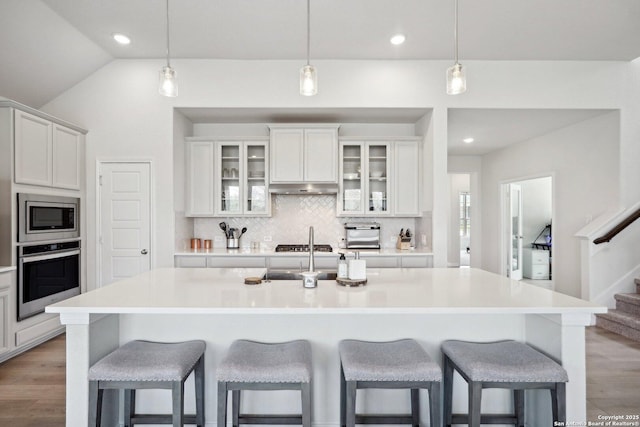 kitchen featuring light wood-type flooring, a breakfast bar, tasteful backsplash, appliances with stainless steel finishes, and lofted ceiling