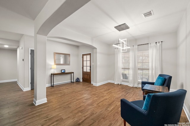 living area featuring baseboards, wood finished floors, visible vents, and arched walkways