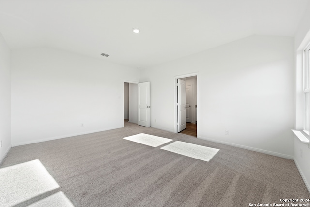 unfurnished bedroom with vaulted ceiling, visible vents, baseboards, and light carpet