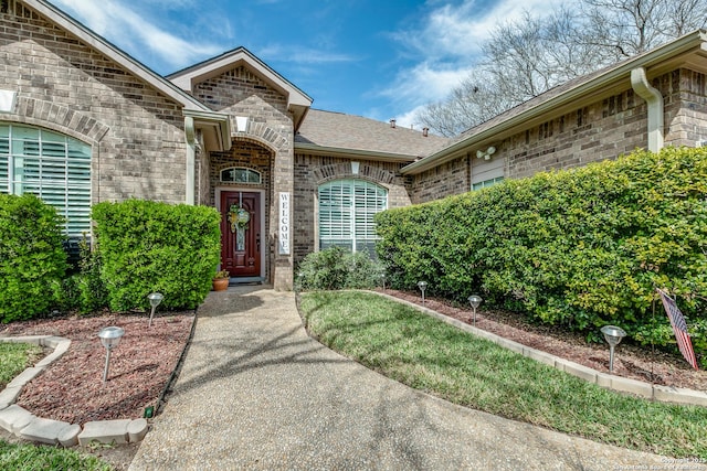 view of exterior entry featuring brick siding and a shingled roof