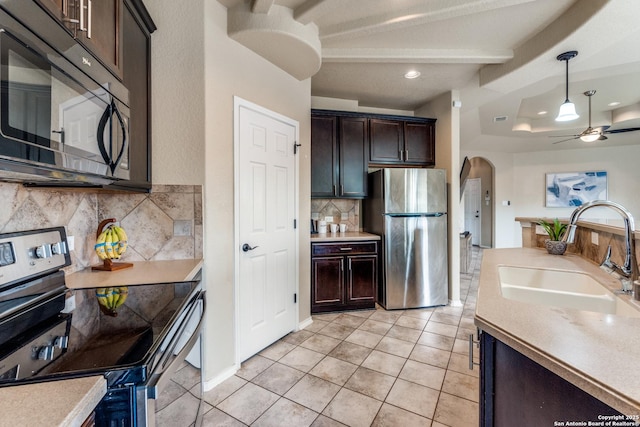 kitchen featuring arched walkways, stainless steel appliances, light countertops, backsplash, and a sink