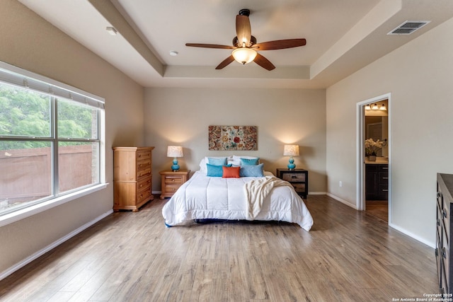 bedroom with a raised ceiling, visible vents, wood finished floors, and baseboards