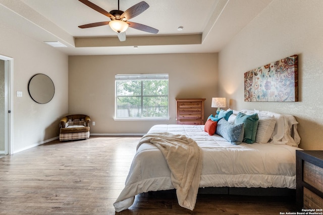 bedroom featuring wood finished floors, ceiling fan, a tray ceiling, and baseboards