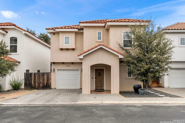 mediterranean / spanish house with stucco siding, driveway, a tile roof, fence, and a garage