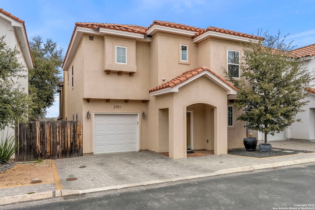 mediterranean / spanish house featuring stucco siding, a tile roof, a garage, and fence