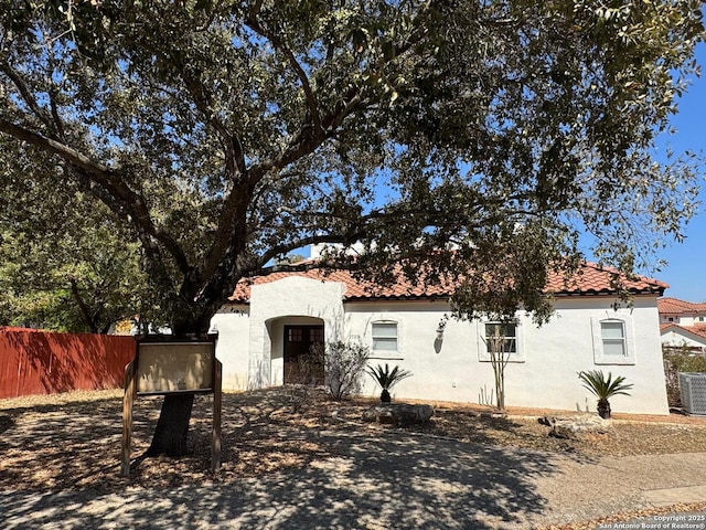 mediterranean / spanish house with a tiled roof, fence, and stucco siding