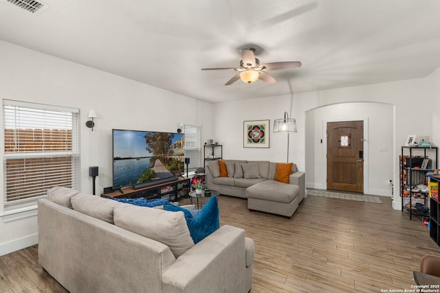 living area with a ceiling fan, baseboards, visible vents, arched walkways, and light wood-type flooring