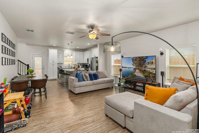 living area with stairs, visible vents, light wood finished floors, and ceiling fan