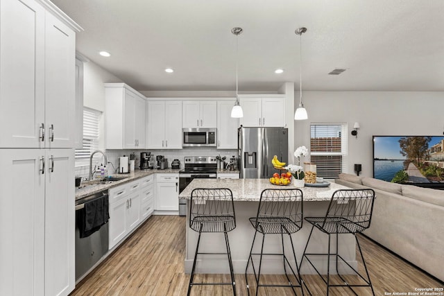 kitchen with a kitchen bar, a sink, wood finished floors, open floor plan, and stainless steel appliances