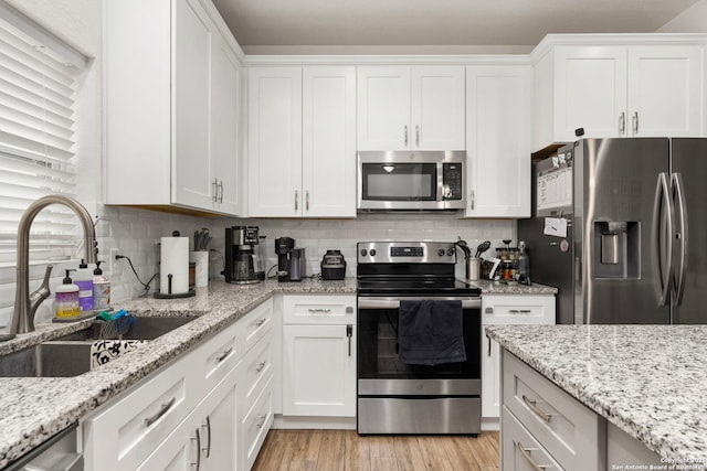 kitchen with light wood finished floors, a sink, stainless steel appliances, white cabinetry, and backsplash