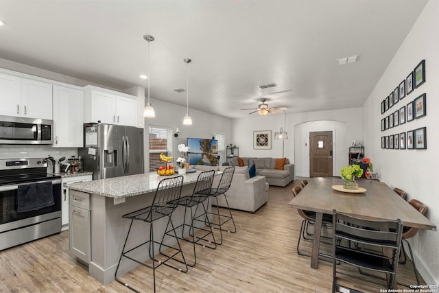 kitchen with light wood finished floors, a kitchen island, appliances with stainless steel finishes, and a breakfast bar area