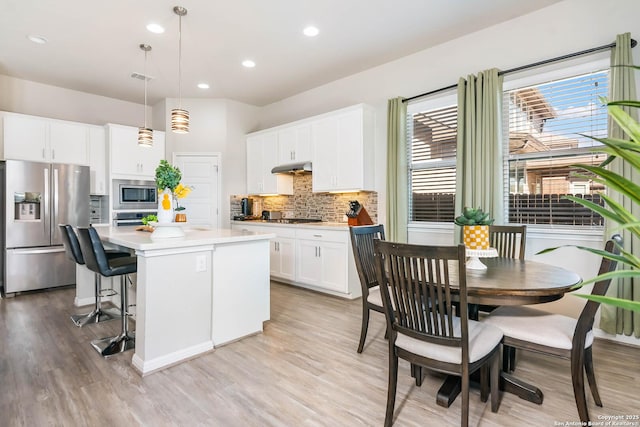 kitchen with tasteful backsplash, a center island, white cabinetry, stainless steel appliances, and light countertops