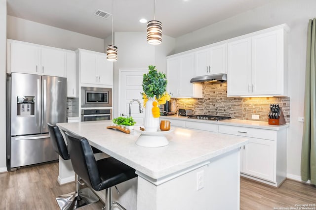 kitchen with visible vents, light countertops, under cabinet range hood, appliances with stainless steel finishes, and backsplash