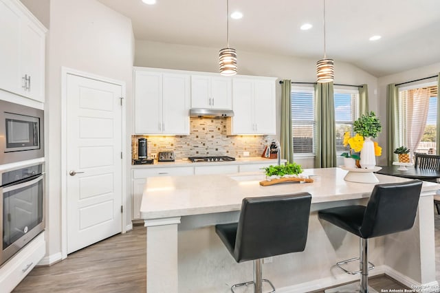 kitchen with a sink, stainless steel appliances, under cabinet range hood, white cabinetry, and backsplash