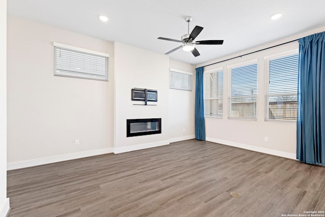 unfurnished living room with a glass covered fireplace, a ceiling fan, baseboards, and wood finished floors