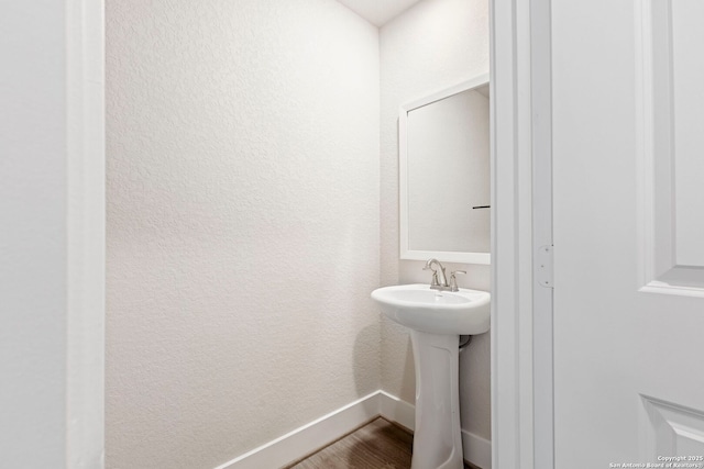 bathroom featuring a textured wall, a sink, baseboards, and wood finished floors