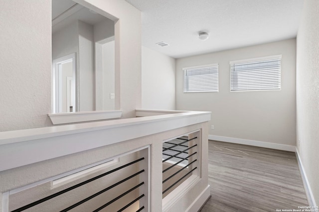 corridor featuring visible vents, wood finished floors, baseboards, and a textured ceiling