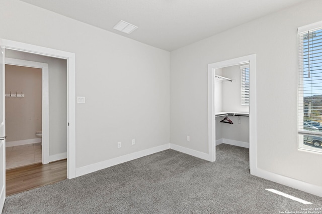 unfurnished bedroom featuring visible vents, multiple windows, a walk in closet, and carpet