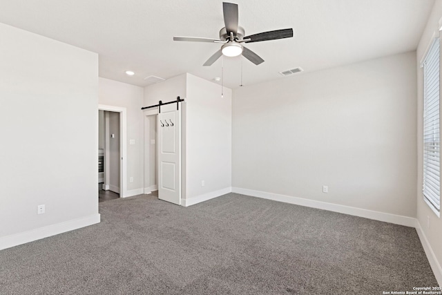 unfurnished bedroom with visible vents, a barn door, carpet flooring, baseboards, and ceiling fan