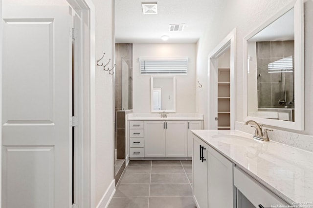 bathroom with tile patterned floors, a tile shower, two vanities, and a sink