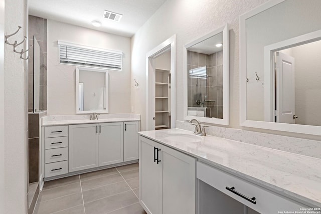 full bathroom featuring tile patterned flooring, visible vents, a tile shower, and a sink