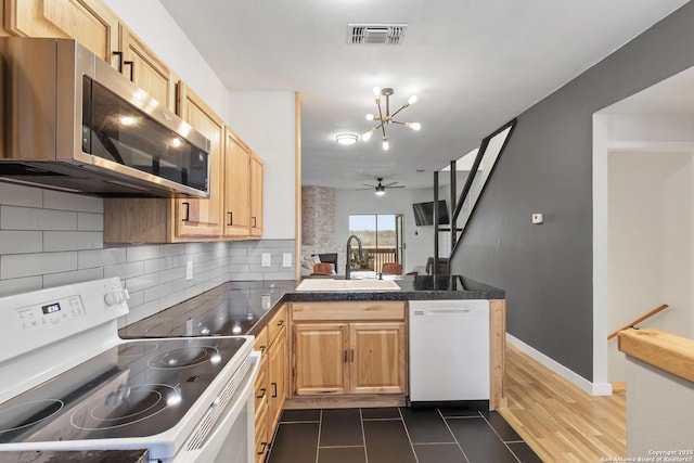 kitchen featuring white appliances, visible vents, a peninsula, a sink, and tasteful backsplash