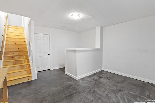 below grade area with stairway, baseboards, and a textured ceiling