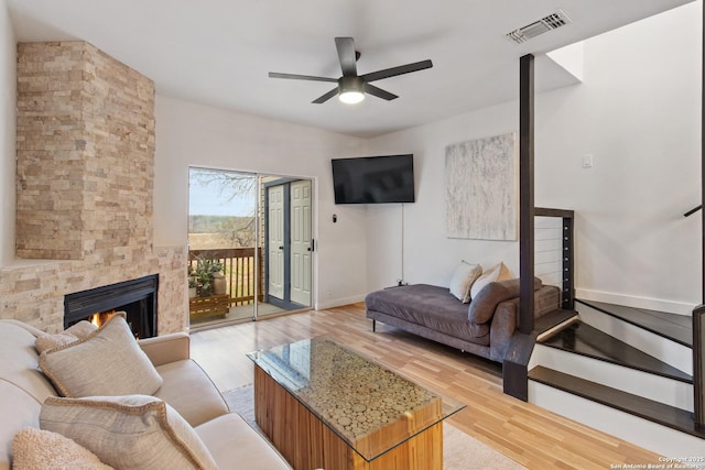 living room featuring visible vents, a ceiling fan, a fireplace, light wood finished floors, and baseboards