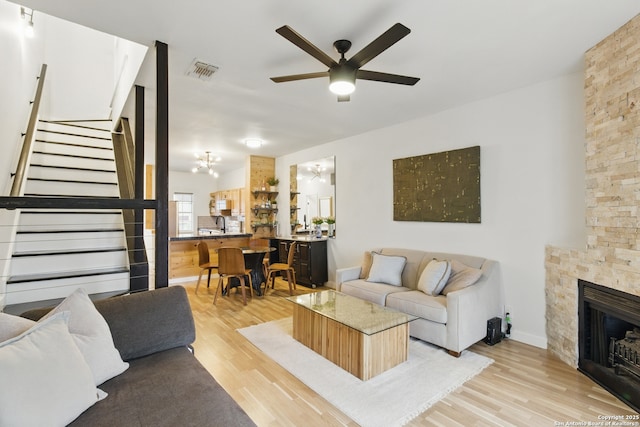 living area with visible vents, light wood-style floors, a fireplace, ceiling fan, and stairs