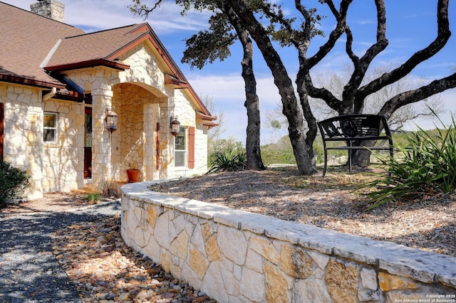 view of side of home with a shingled roof, stone siding, and a chimney