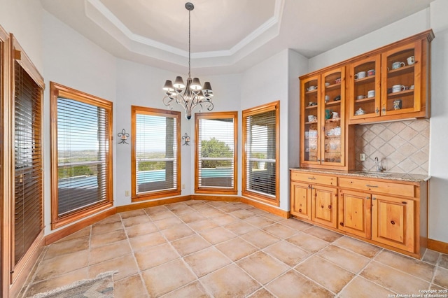 unfurnished dining area featuring baseboards, a raised ceiling, a healthy amount of sunlight, and an inviting chandelier