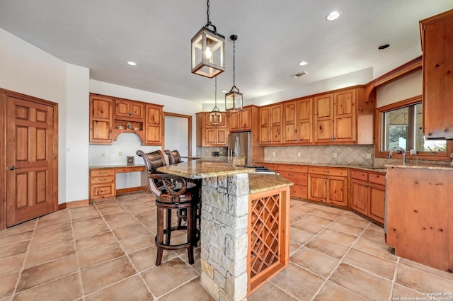 kitchen featuring tasteful backsplash, light stone counters, brown cabinets, appliances with stainless steel finishes, and hanging light fixtures