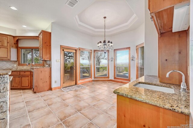 kitchen featuring visible vents, a sink, a tray ceiling, decorative backsplash, and light stone countertops