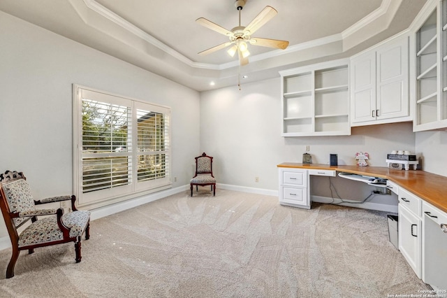 office space featuring a ceiling fan, a tray ceiling, baseboards, light colored carpet, and built in study area