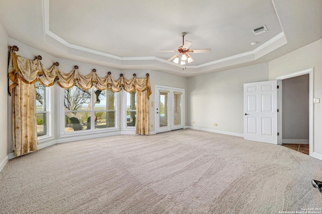 carpeted empty room featuring a tray ceiling, baseboards, visible vents, and ceiling fan