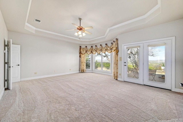 carpeted empty room with a tray ceiling, baseboards, visible vents, and a ceiling fan