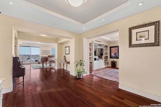 hall with built in shelves, a raised ceiling, wood finished floors, recessed lighting, and baseboards