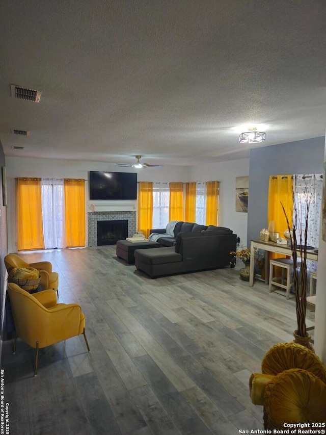 living area with visible vents, ceiling fan, a tiled fireplace, wood finished floors, and a textured ceiling