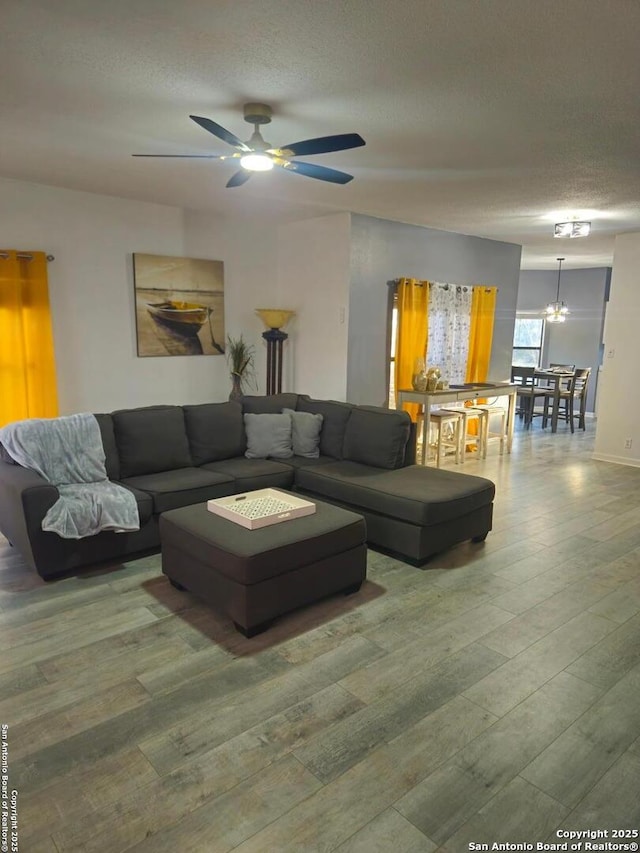 living area with ceiling fan with notable chandelier, a textured ceiling, and wood finished floors