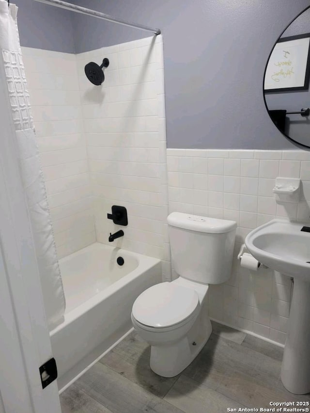 bathroom with wood finished floors, shower / bath combo, wainscoting, tile walls, and toilet