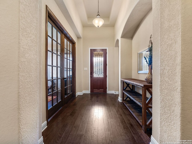 entrance foyer featuring baseboards, a tray ceiling, french doors, hardwood / wood-style flooring, and arched walkways