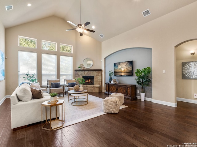 living room featuring visible vents, wood finished floors, arched walkways, a stone fireplace, and ceiling fan