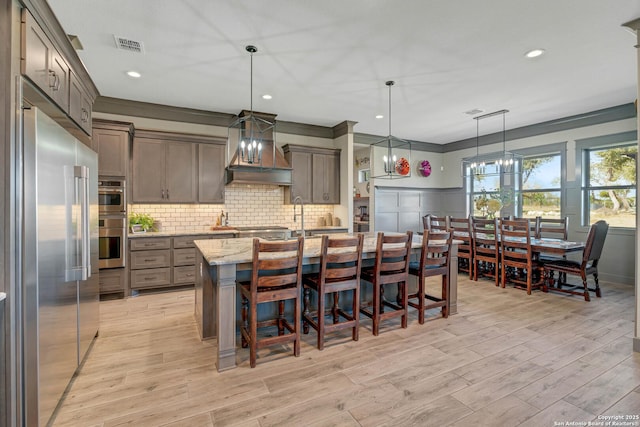 kitchen featuring visible vents, an island with sink, light stone counters, tasteful backsplash, and appliances with stainless steel finishes