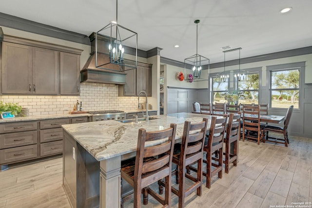 kitchen with tasteful backsplash, a chandelier, light stone counters, light wood-style flooring, and a sink