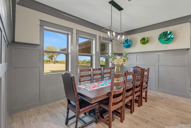 dining area with a chandelier, a decorative wall, crown molding, and light wood-type flooring